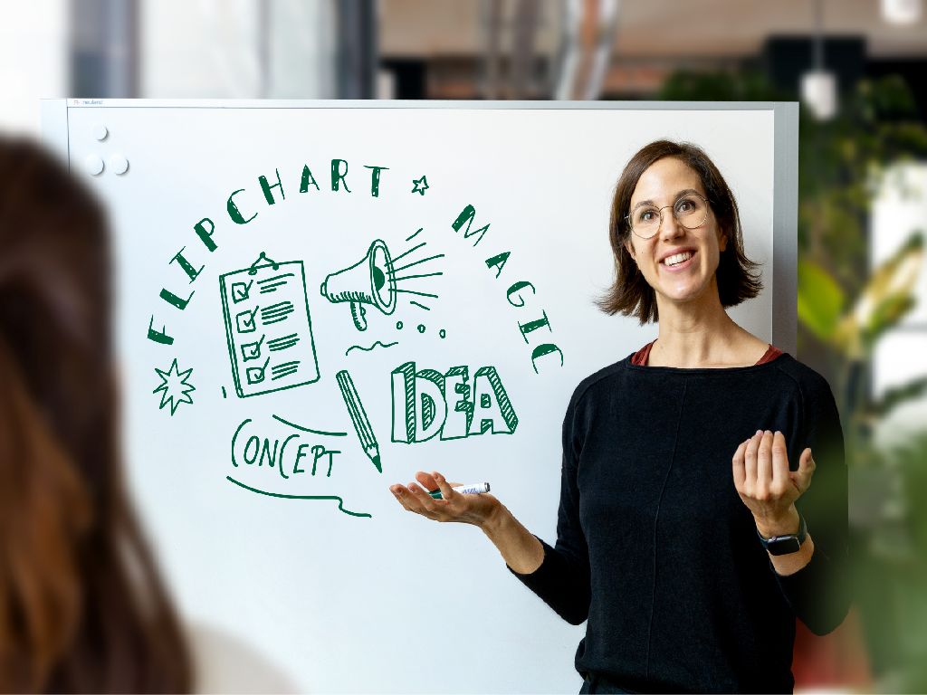 Referentin Antonia Horvath steht vor einem Whiteboard mit grünen Skizzen zu 'Flipchart', 'Idee', 'Konzept' und weiteren Stichwörtern, während sie gestikulierend präsentiert - symbolisiert interaktive Lehr- und Moderationsmethoden.