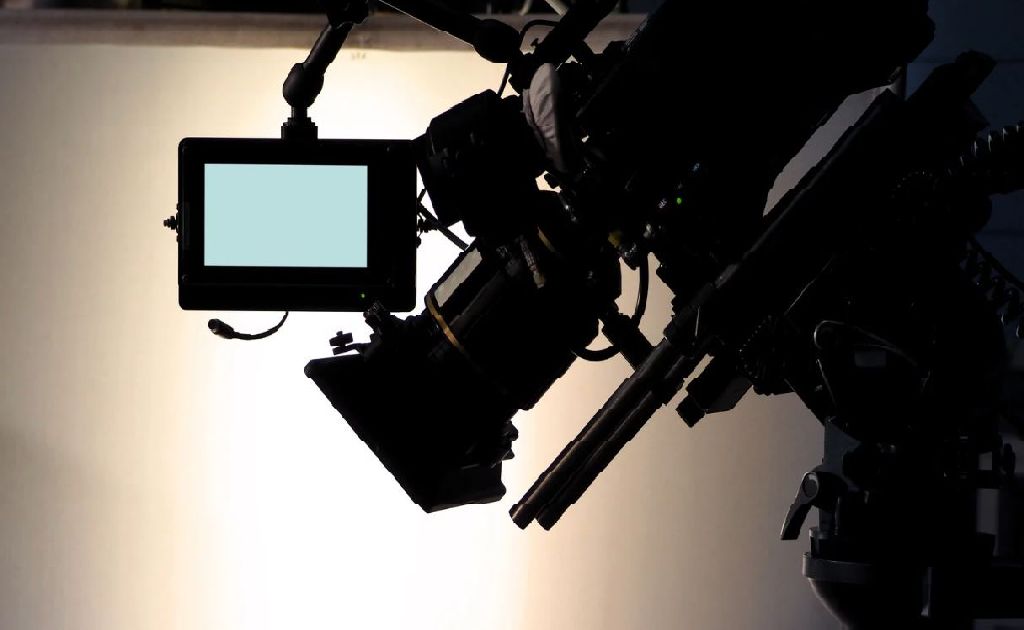 Silhouette einer professionellen Filmkamera mit Monitor im Gegenlicht - symbolisiert Videoproduktion und mediale Aufbereitung von Lehrinhalten.