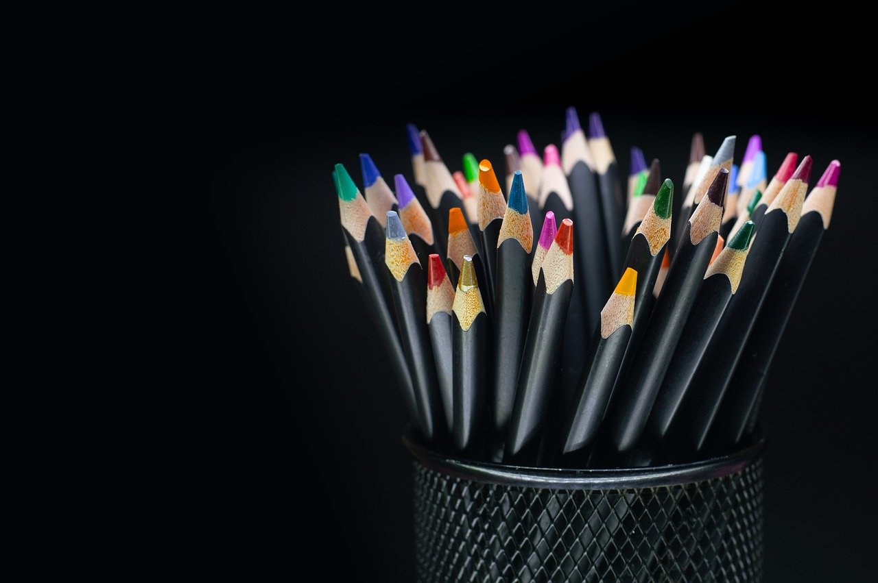 Learning Design Bunte Buntstifte mit verschiedenfarbigen Spitzen in einem schwarzen Stifthalter vor dunklem Hintergrund - symbolisiert Kreativität, Vielfalt der Gestaltungsmöglichkeiten und die methodische Werkzeugvielfalt im Learning Design.