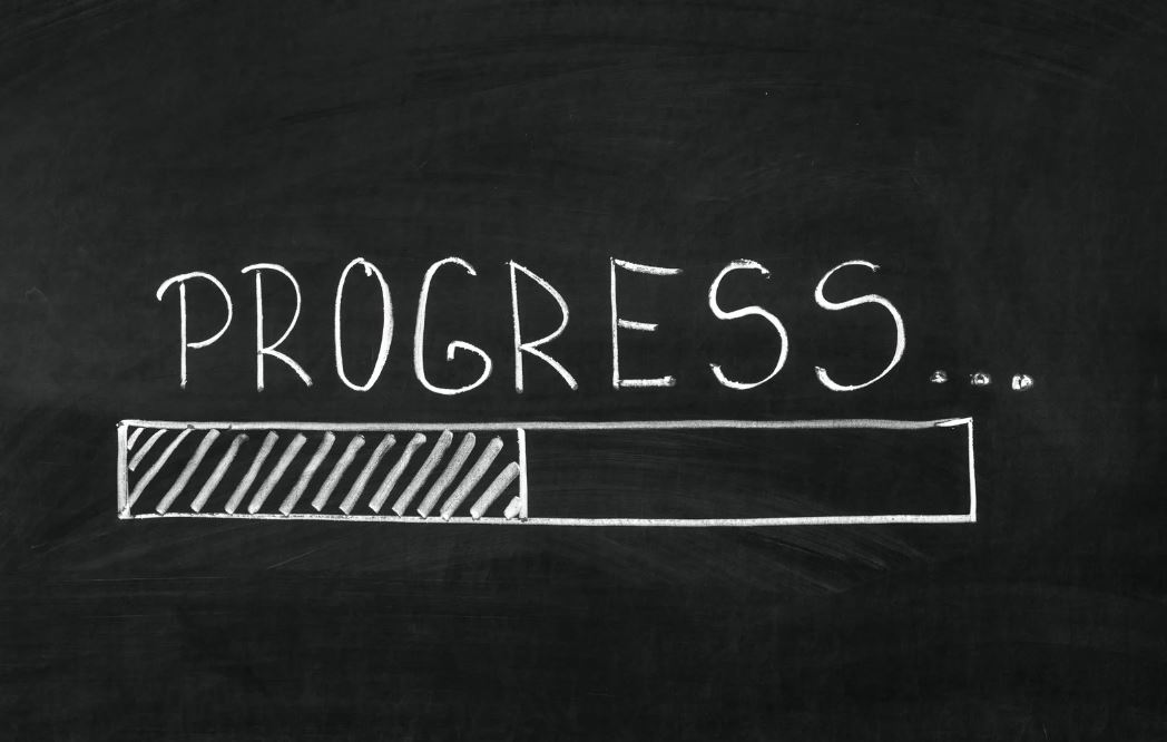 Tafel mit Kreideschrift 'PROGRESS' und einem sich füllenden Fortschrittsbalken - symbolisiert kontinuierliche Lernentwicklung, Feedback und die schrittweise Unterstützung des Lernfortschritts durch formatives Assessment.