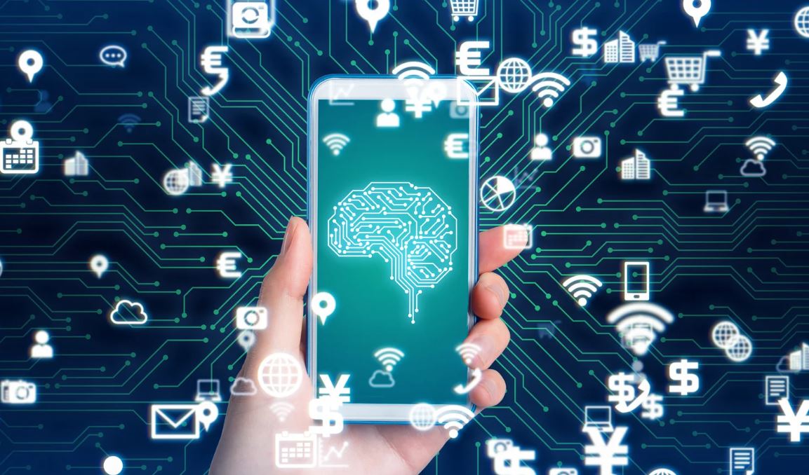 "Hand hält Smartphone mit leuchtendem Gehirn-Symbol auf dem Display, umgeben von schwebenden digitalen Icons wie Cloud, Personen und Kommunikationssymbolen - symbolisiert die Förderung von KI-Kompetenz und digitalen Fähigkeiten bei Studierenden in der Hochschullehre.