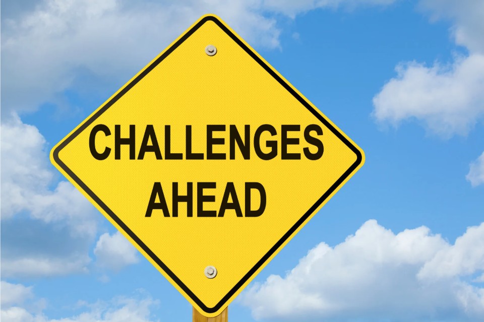 Gelbes Warnschild mit der Aufschrift 'CHALLENGES AHEAD' vor blauem Himmel mit weißen Wolken - symbolisiert die Vorbereitung auf und den professionellen Umgang mit schwierigen Situationen im Lehralltag.